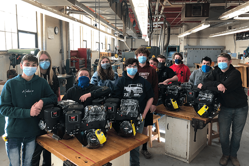 Group of masked students in workshop with black backpacks